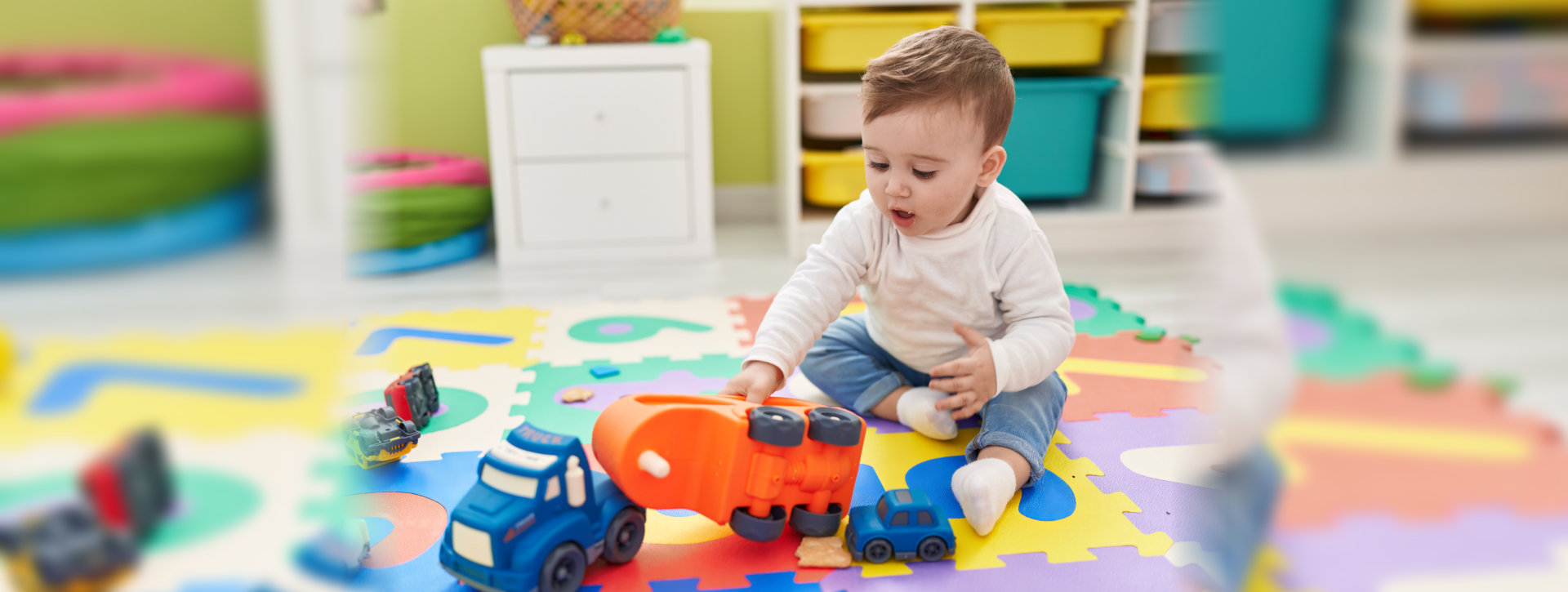  baby playing with truck toy sitting on floor at kindergarten
